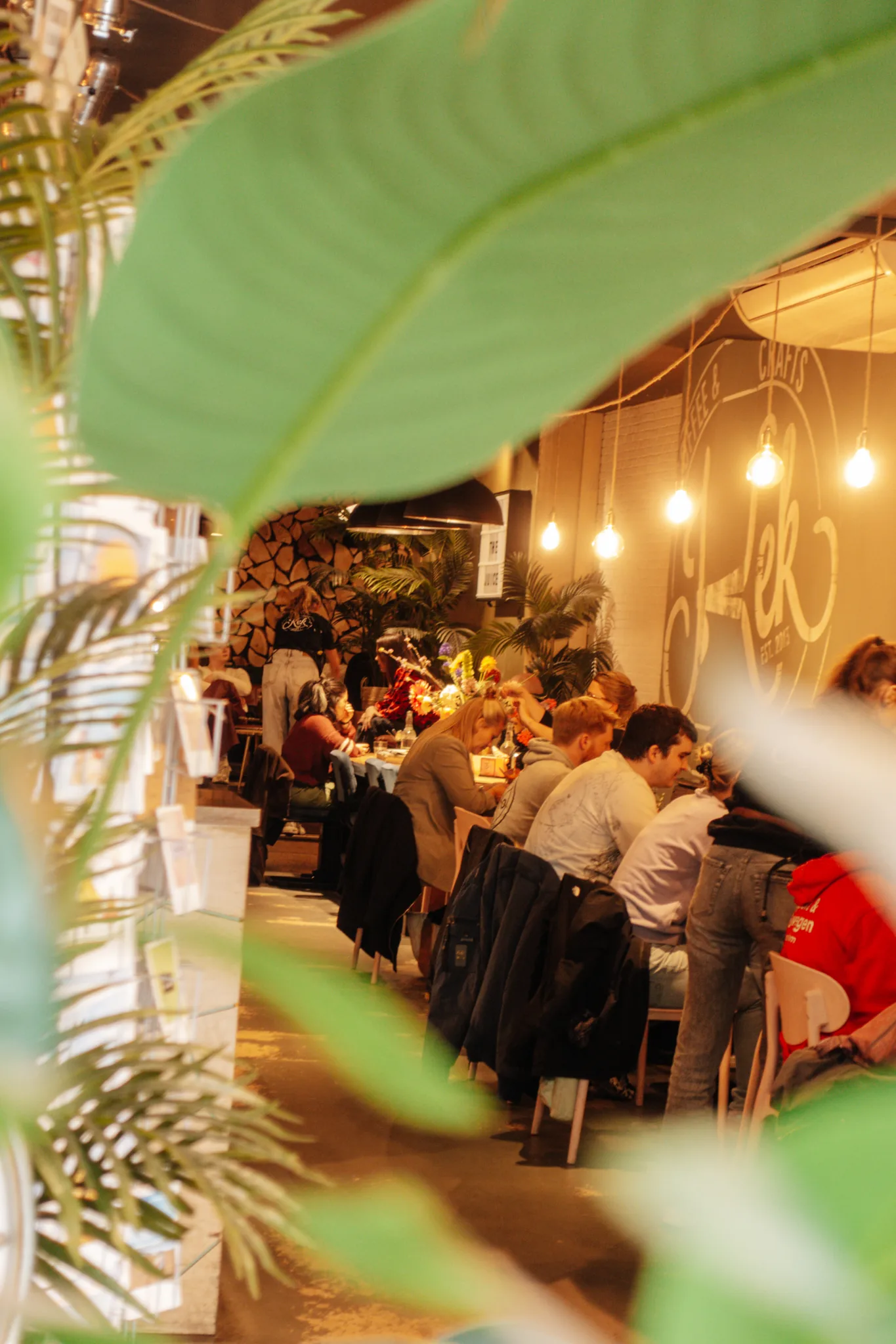 Gasten aan tafel in de koffiebar van Kek, tussen de planten
